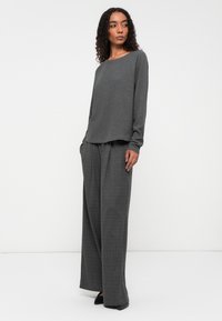 Grijze longsleeve shirt met een ontspannen pasvorm; gecombineerd met hoog-waist, wijde geruite broek in grijstinten en zwart, met een gladde textuur.