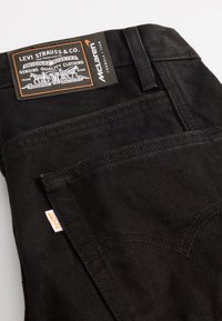 Black denim jeans featuring a Levi Strauss & Co. label, McLaren branding, and accent stitching on the back pocket with a small orange tag.