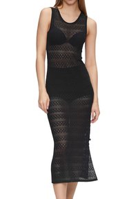 Musta neulemekko, jossa on istuva siluetti, geometrinen kuvio, hihaton malli, puolipitkä pituus ja hieman läpinäkyvä materiaali.