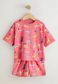 Ensemble rose pour enfants comprenant une chemise à manches courtes et un short avec des motifs colorés de chien, cœur et os dessinés, suspendu à un cintre en bois.