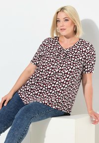 Blouse à manches courtes noire avec un motif de cœurs blancs et rouges. Design à col en V avec une coupe décontractée. Associée à un jean en denim bleu.