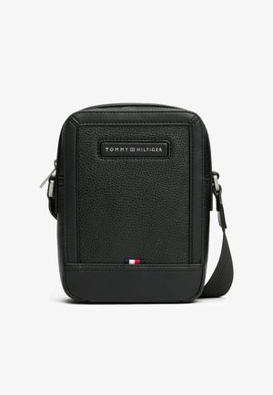 Sort tekstureret læder skuldertaske med lynlås, med et frontlogo og en tri-farvet accent nederst.