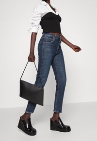 Top corto de canalé negro, vaqueros oscuros de corte ajustado y zapatos de cuña negros brillantes. Sosteniendo un bolso rectangular negro.