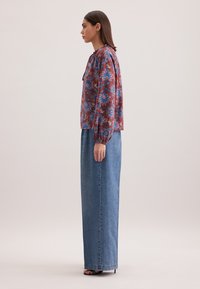 Blusa floreale a maniche lunghe rossa con motivi blu e bianchi, abbinata a una gonna in denim a vita alta arriva alla caviglia e sandali neri con tacco.
