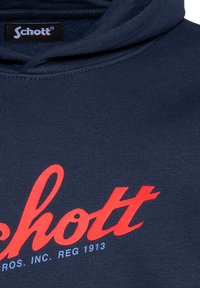 Felpa blu navy con un grande logo rosso "schott" con dettagli bianchi. Texture liscia, cappuccio regolabile e polsini e orlo a costine.