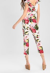 Floral jumpsuit with short ruffled sleeves, featuring a vibrant mix of pink, red, and yellow flowers on a white background. Ankle-length fit.