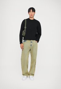 Felpa nera con logo in rilievo, jeans a righe verdi chiari a gamba larga, sneakers bianche e una borsa a tracolla verde oliva.