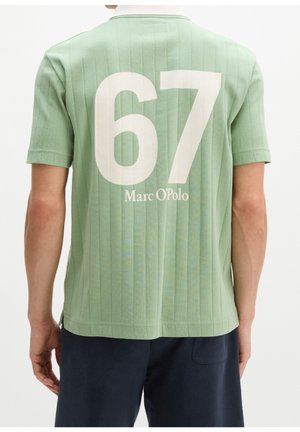Homme portant une chemise vert clair à manches courtes avec le numéro blanc 67 et le texte "Marc O'Polo" au dos, associé à un short foncé.