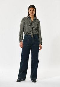 Svart och vit mönstrad blus med slipskrage, bärs med high-waisted mörkblå vida byxor med framfickor och gula sömmar.