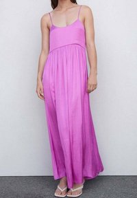 Robe maxi en tissu dégradé rose, dotée de fines bretelles, d'un corsage ajusté et d'une jupe fluide. Texture lisse avec un tomber naturel.
