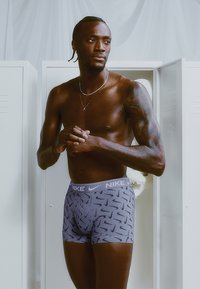 Nike boxershorts i lys grå med et gjentagende mønster av mørkegrå swoosh. Stoffet ser glatt ut med en elastisk linning merket "NIKE."