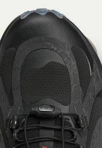 Black sneaker with a textured upper, featuring smooth leather and mesh panels. Includes black laces and a red accent on the tongue.