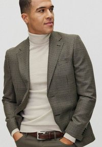 Brązowy blazer w kratę houndstooth z wyciętymi klapami, noszony na kremowym golfie. Brązowy pasek kontrastuje z oliwkowymi spodniami.