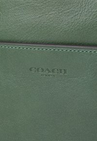 Portafoglio in pelle verde con logo goffrato "COACH NEW YORK", cuciture a contrasto e superficie texturizzata per una maggiore durabilità.