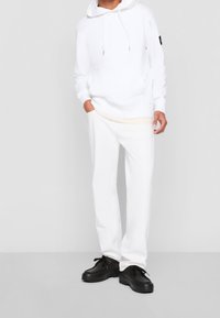 Vit hoodie med snören, matchad med vita byxor. Svarta skor med snören och tjock sula. Minimalistisk design, slät yta.