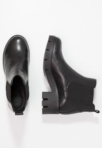 Botas de cuero negro hasta el tobillo con paneles laterales elásticos, punteras redondeadas y tacones gruesos con cortes verticales en la parte posterior.