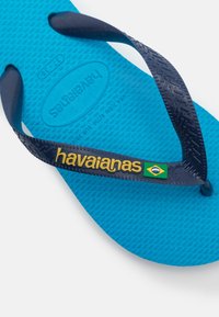 Modra gumijasta natikača s temno modrimi trakovi. Ima teksturirano podplato in blagovno znamko "havaianas" z akcentom brazilske zastave.
