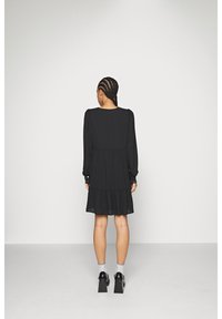 Robe noire courte avec de longues manches bouffantes, une jupe à volants et des boutons sur les poignets. Tissu léger avec un design fluide.