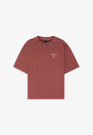 Koszulka w kolorze rdzawego brązu z krótkim rękawem, z napisem "SALSA CLUB HAVANA CUBA" na lewej stronie klatki piersiowej, z okrągłym dekoltem i luźnym krojem.