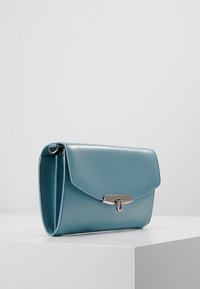 Ljusblå läderhandväska med en strukturerad siluett, lockstängning, silverfärgade detaljer och slät textur.