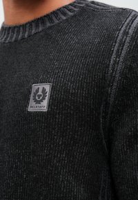 Melnā adīta džemperis ar teksturētu rakstu, ar ribotu apkakli un mazu pelēku Belstaff logu uz krūšu daļas.
