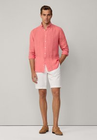 Camicia button-up di lino corallo, con maniche arrotolate, abbinata a pantaloni corti bianchi e mocassini beige. Design semplice con vestibilità rilassata.