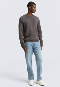 Szürke kötött pulóver kerek nyakkivágással és bordázott mandzsettákkal, világoskék farmerrel és fehér sportcipővel párosítva. Sima textúra, laza szabás.