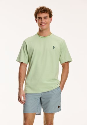 Light green short-sleeve t-shirt with a small dark green logo on the chest, paired with navy and white striped shorts featuring a logo patch.