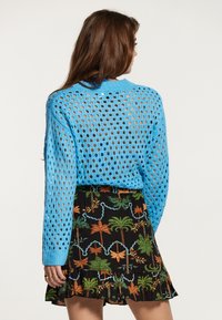 Maglione blu lavorato a maglia con un motivo a rete aperta e maniche lunghe, abbinato a una gonna nera con stampa di foglie tropicali e volant.