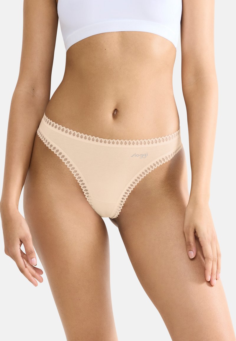 Beige stringtangas met decoratieve kantafwerking langs de tailleband en beenopeningen; zachte, gladde stoftextuur met minimale branding.