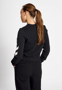 Czarny sweatshirt z długimi rękawami, okrągłym dekoltem, prążkowanym wykończeniem i białymi ukośnymi paskami na rękawach, wykonany z miękkiego, strukturalnego materiału.