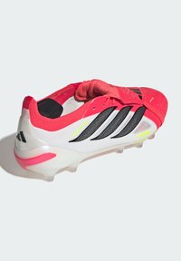 Κόκκινο και λευκό ποδοσφαιρικό παπούτσι Adidas Predator με μαύρες ρίγες και καλουπωμένες τάπες σε λευκό φόντο.