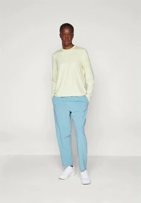 Light yellow long-sleeve top paired with light blue trousers and white sneakers. The outfit features a relaxed fit and smooth texture.