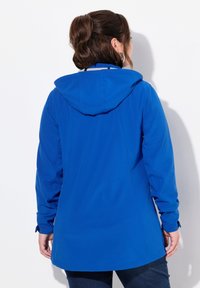 Veste à capuche bleue avec une texture lisse, dotée de manches longues et d'une coupe droite. Les détails incluent des poignets ajustables et un design sans coutures.