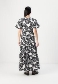 Maxiklänning med svart blommönster på vit bakgrund. Har puffärmar, en lagerdesign och en lös passform. Svarta ankelboots är på. 