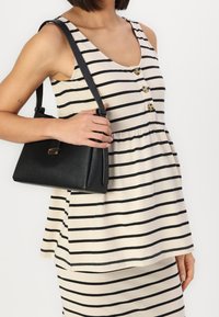 Black textured handbag with a structured design and gold hardware, held by a person wearing a cream-striped sleeveless dress.