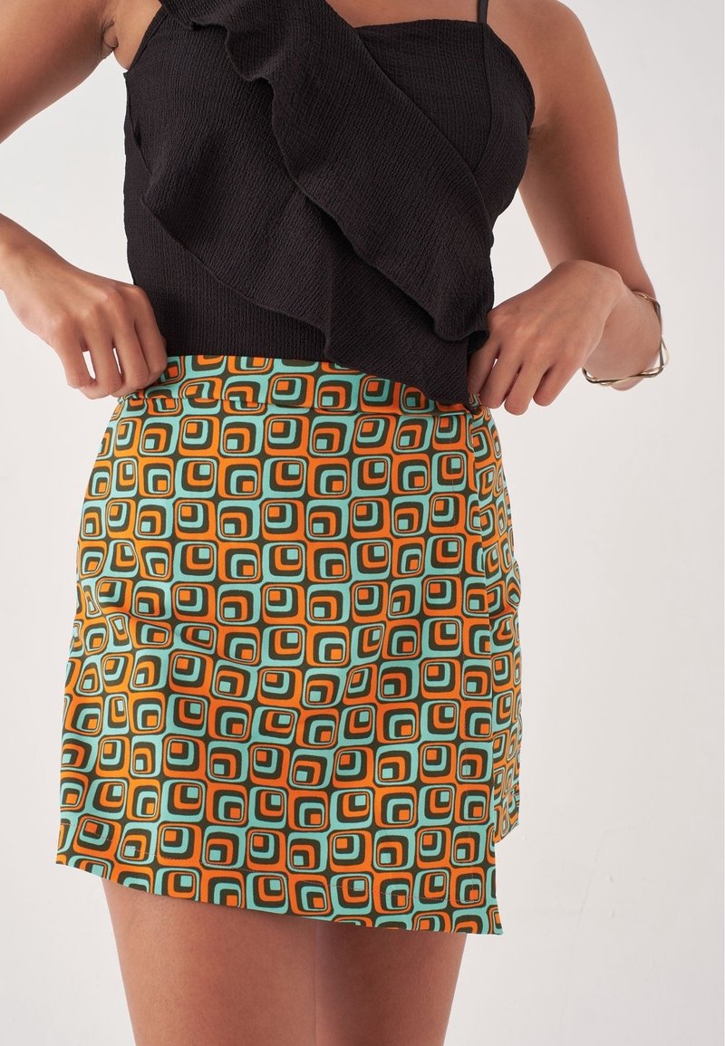 Haut noir côtelé avec volants associé à une mini-jupe multicolore arborant un motif géométrique en bleu sarcelle, orange et noir.