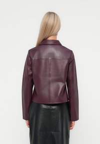 Veste en cuir bordeaux au design ajusté, texture lisse, et col à revers, associée à une jupe en cuir noire.