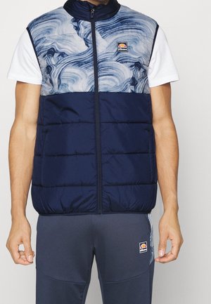 Veste sans manches matelassée avec un motif abstrait bleu sur la moitié supérieure, moitié inférieure unie bleu marine, associée à un pantalon de survêtement bleu marine, les deux avec logos Ellesse.
