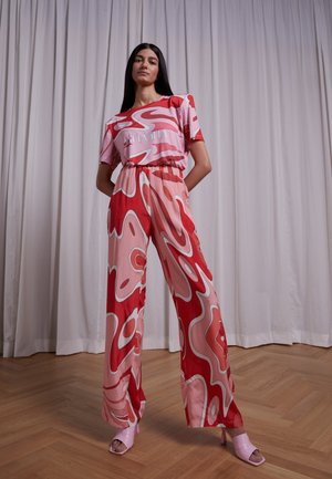 Conjunto de duas peças composto por uma blusa rosa de mangas curtas com padrões abstratos brancos e calças rosa de cintura alta com um design semelhante.