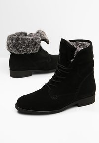 Bottines en daim noir avec poignets en fausse fourrure, design à lacets, talon plat et coutures détaillées sur les côtés.