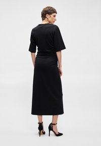 Μαύρο maxi φόρεμα με κοντά μανίκια, εφαρμοστό κορσέ και ραφές στη μέση. Φορεμένο με μαύρες ψηλές γόβες με λουράκια στον αστράγαλο.