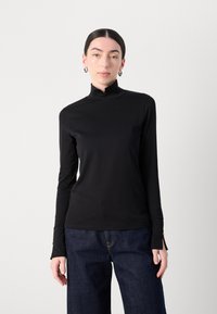 Zwarte lange mouw top met een hoge kraag, met een aansluitend ontwerp, gladde textuur en subtiele stikseldetails. Gecombineerd met losse denim broeken.