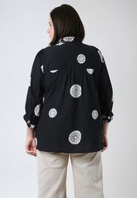 Black shirt with white floral embroidery; features a collar, three-quarter sleeves with rolled cuffs, and a loose fit design.