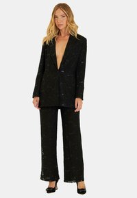 Zwarte kanten pak met pailletten, bestaande uit een blazer met diepe V-hals en een broek met rechte pijpen. Glad textuur, gedetailleerd patroon overal.
