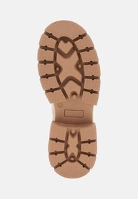 Suola in gomma color beige con superficie testurizzata e a motivo per una presa migliore, dotata di un logo centrale e di un design del battistrada sagomato per una maggiore aderenza.