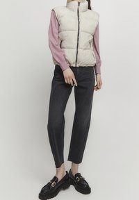 Pufferväst i krämfärg, långärmad rosa topp, svarta raka jeans, kraftiga svarta loafers med detaljer i guldspänne. Avslappnat alternativ.