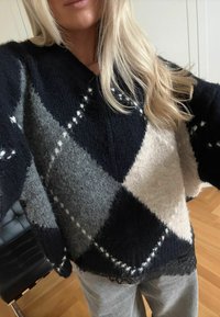 Sweter w czarne, szare i kość słoniową wzory w romby, wykonany z miękkiego dzianinowego materiału z koronkową lamówką u dołu. Luźny krój z dekoltem w kształcie litery V.