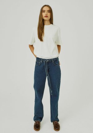 Vitt t-shirt med kort ärm i kombination med högmidjade blå denimjeans och bruna oxfordskor, med en avslappnad passform och minimalistisk design.
