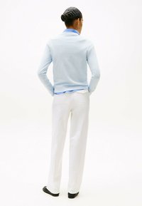 Maglione azzurro chiaro a maniche lunghe con colletto, abbinato a pantaloni bianchi a gamba dritta e scarpe flat nere, visto da dietro.